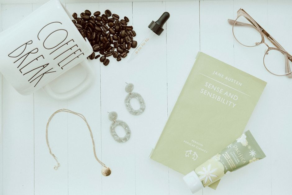 Aesthetic flat lay featuring coffee, book, jewelry, and skincare.