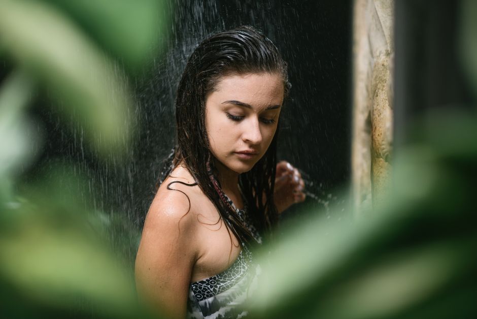 Young gorgeous long haired brunette enjoying shower at spa resort full of vibrant tropical greenery