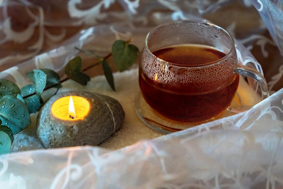 A peaceful tea setup with a glass teacup, stone candle, and eucalyptus leaves, perfect for relaxation.