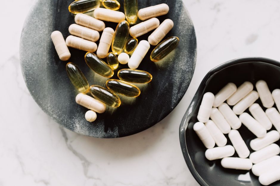 Top view of biologically active additives include tablets and capsules placed in ceramic bowl and on stone stand against marble board