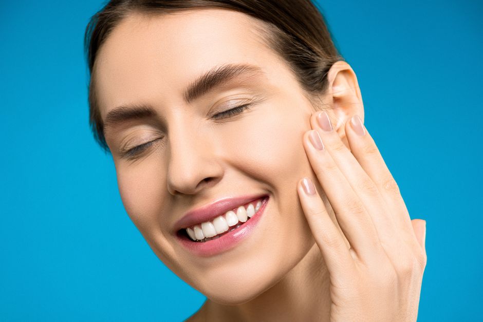 Portrait of a smiling woman with closed eyes against blue background.