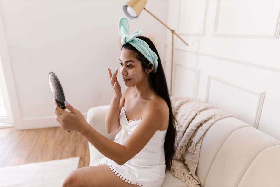 A woman applies makeup while seated on a couch in a cozy room, reflecting self-care routines.