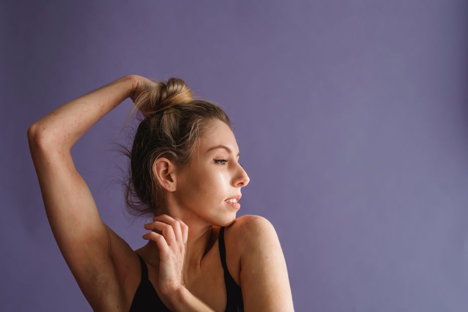 Tranquil young woman standing with raised arms and looking away against purple background in studio