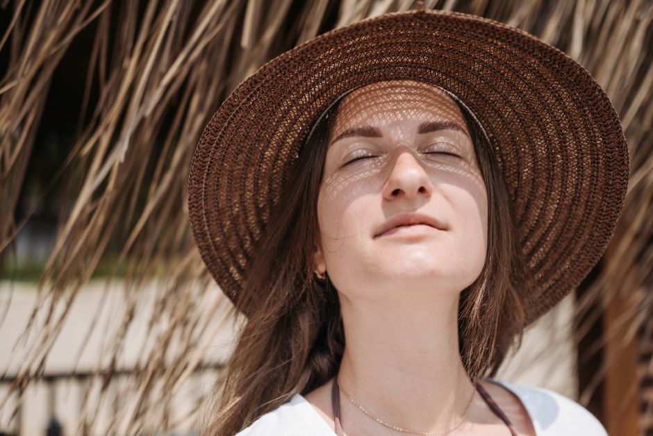 Close-up portrait of a woman with eyes closed, wearing a sunhat, enjoying sunlight.