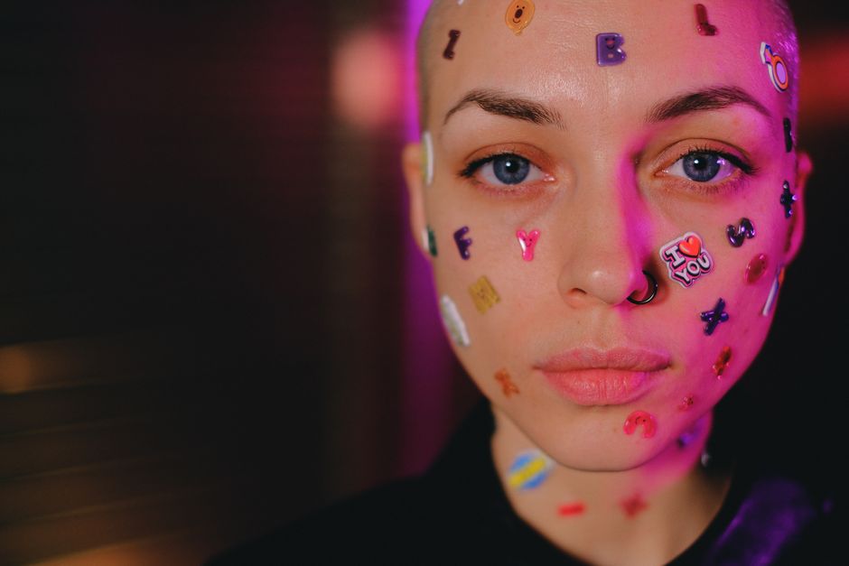 Crop calm bald female with letter stickers on face standing in dark studio and looking at camera
