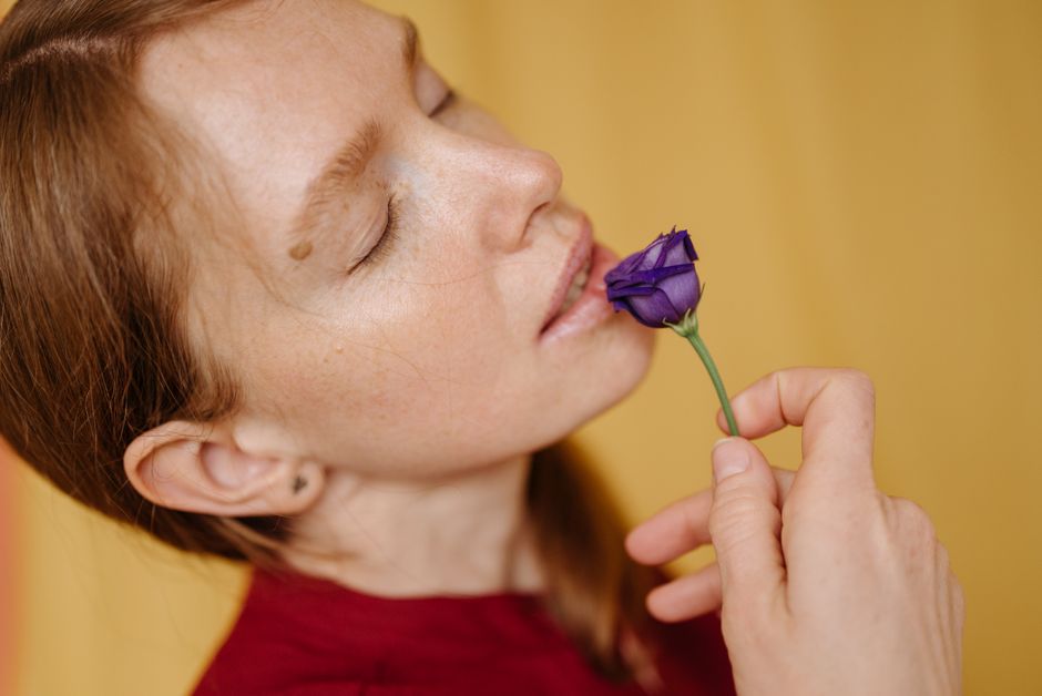 Close-up of a woman with freckles in red, holding a purple flower and closing her eyes.