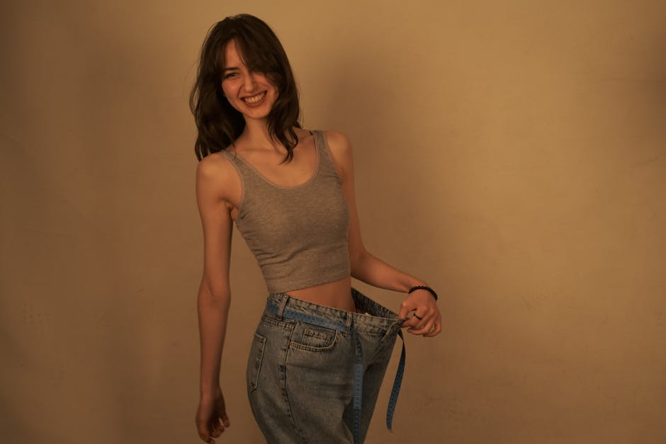 Joyful woman shows success in weight loss by wearing loose jeans. Healthy lifestyle concept.