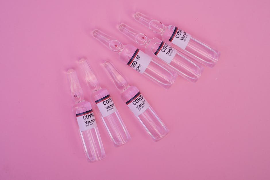 Top view set of sealed glass ampoules with COVID 19 vaccine arranged on pink surface