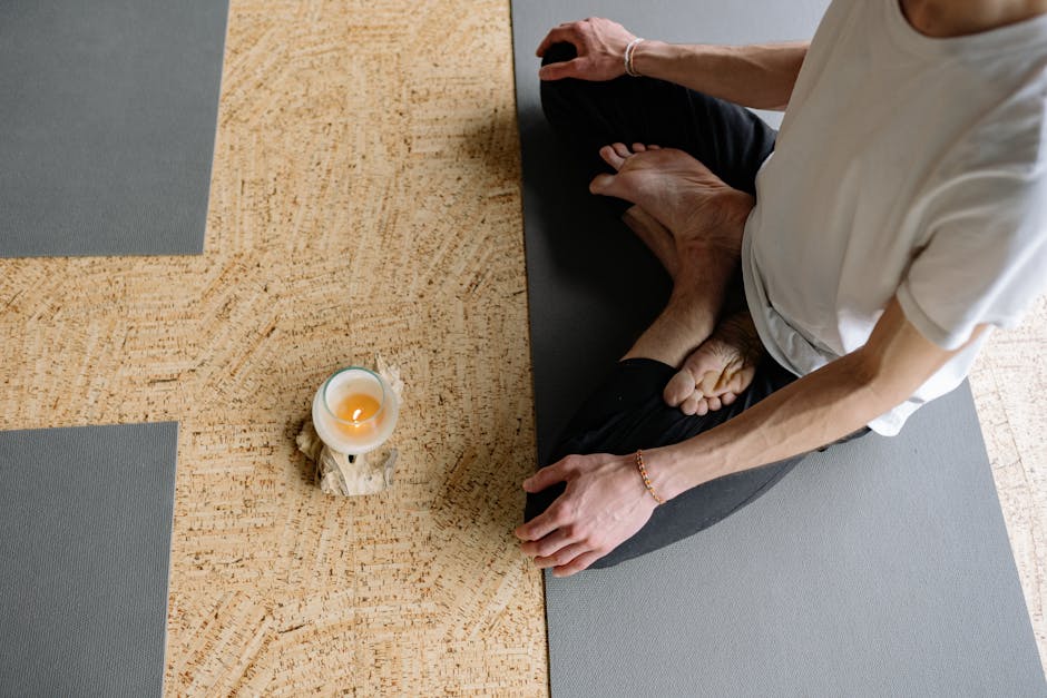 Adult meditating in lotus pose on yoga mat with candle, creating a calming atmosphere.