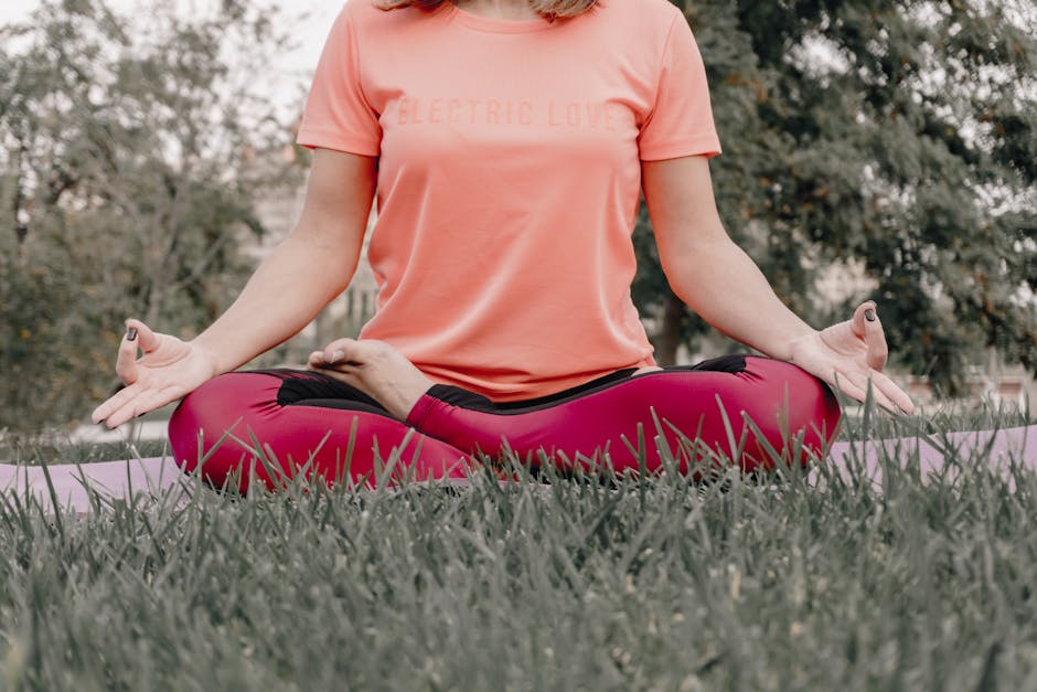 Woman practicing yoga in lotus position outdoors on grass, promoting mindfulness and relaxation.