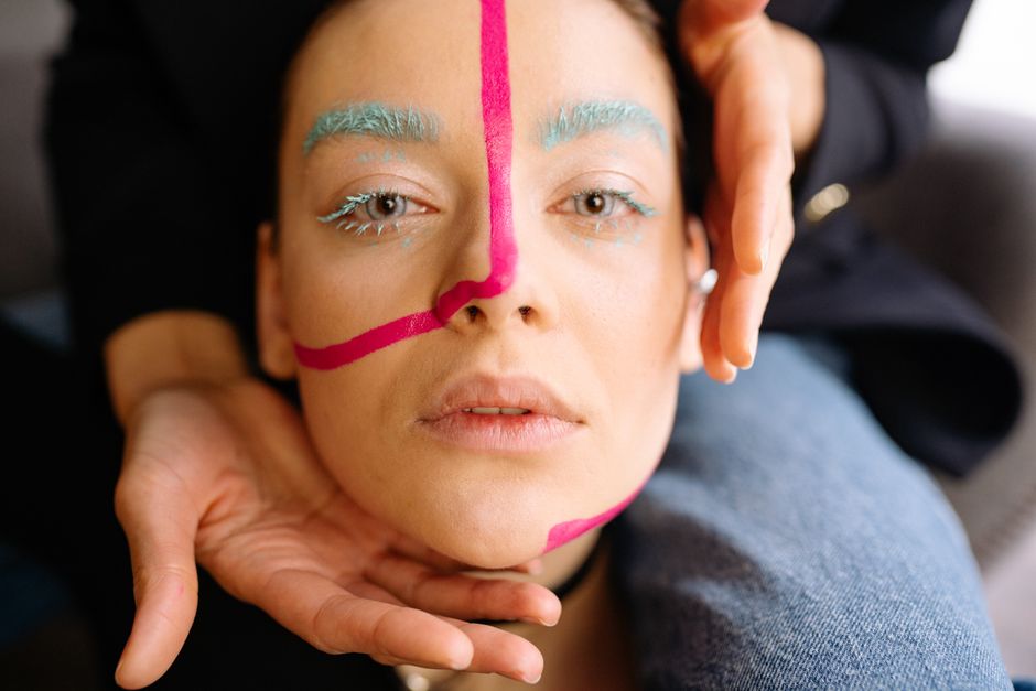 Close-up portrait highlighting creative makeup with hands framing a woman's face artistically.
