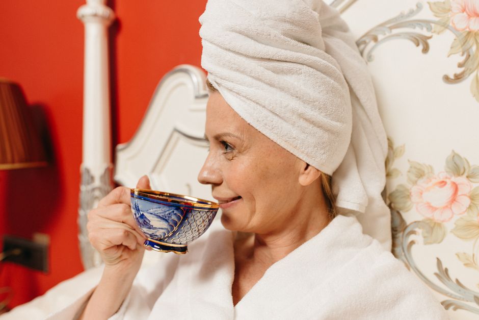 Elegant portrait of a woman enjoying her drink with a towel on her head, in a cozy and stylish room.