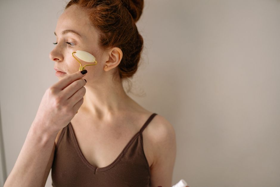 A woman applying a jade face roller as part of her skincare routine, promoting self-care.