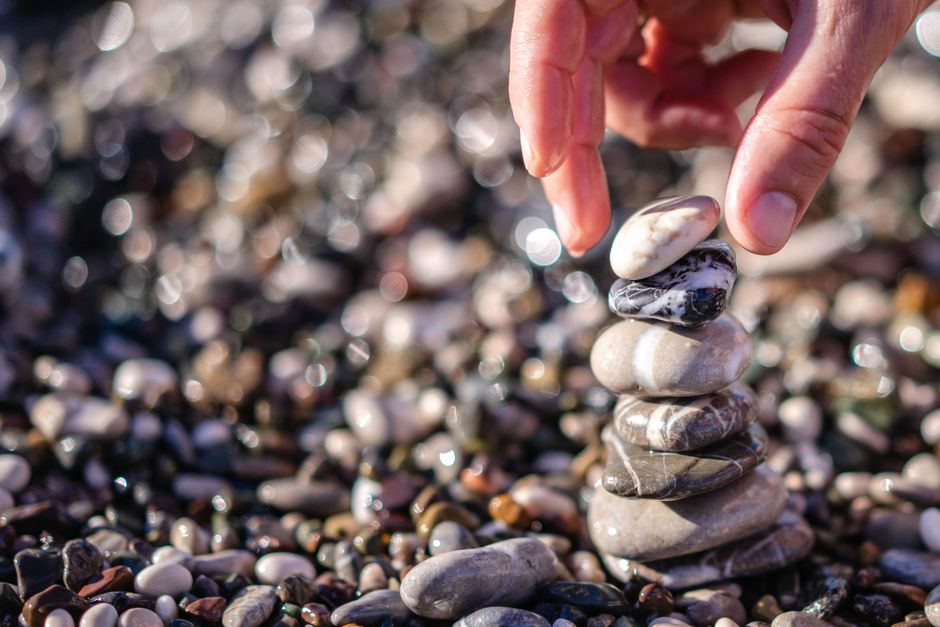 A hand carefully stacks smooth stones outdoors, symbolizing balance and tranquility.