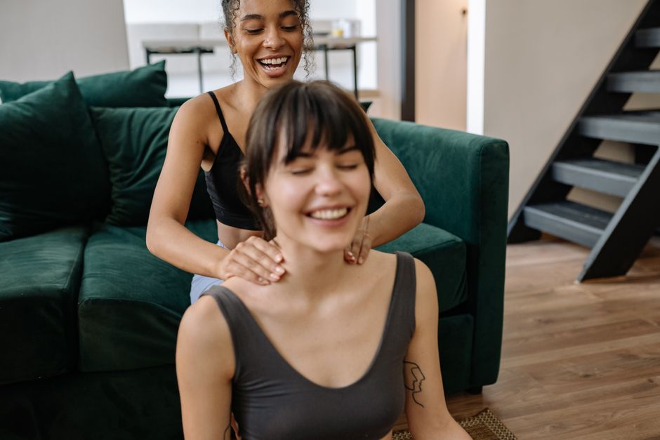Two women enjoy a relaxing neck massage at home, highlighting friendship and wellness.