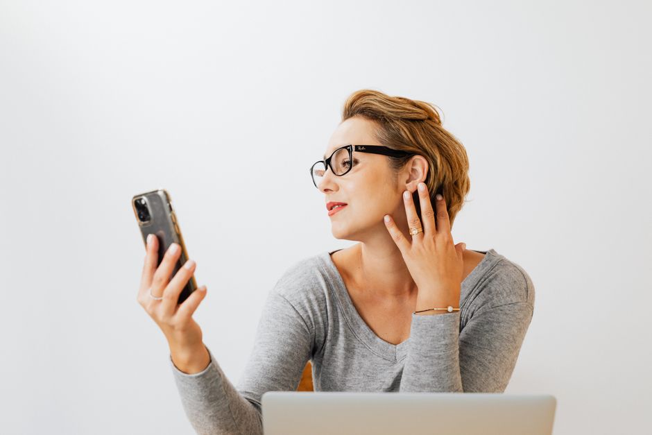 Caucasian woman with eyeglasses and light background taking a selfie indoors.