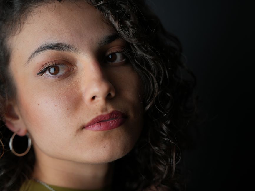 A striking close-up portrait of a woman with curly hair, large earrings, and a pensive expression.