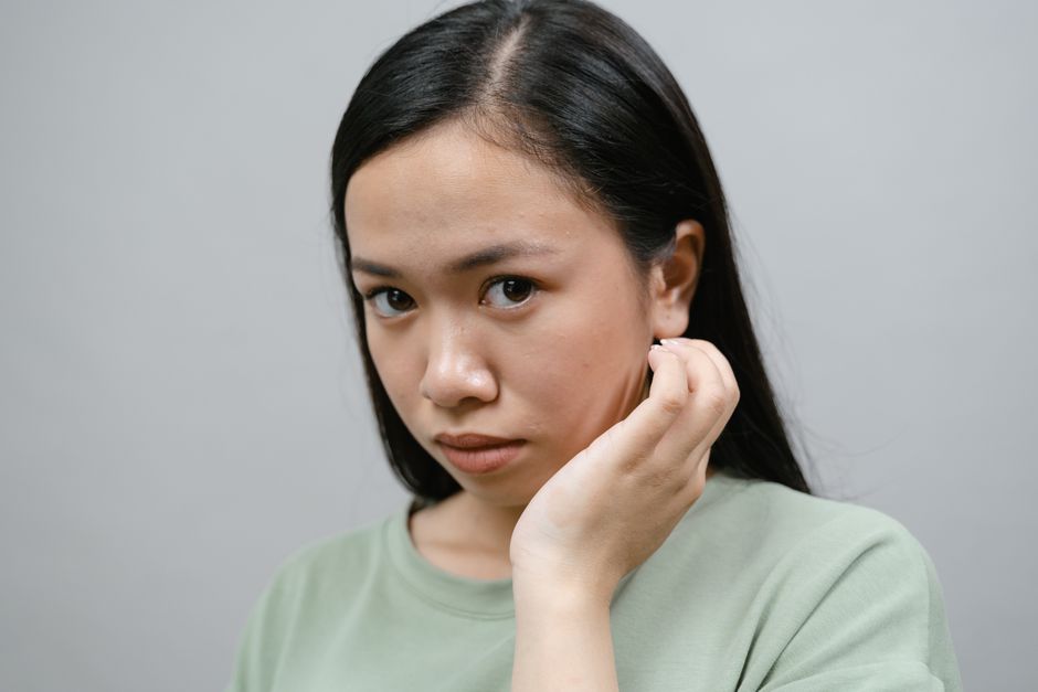 Close-up portrait of an Asian woman in a green shirt with a thoughtful expression.
