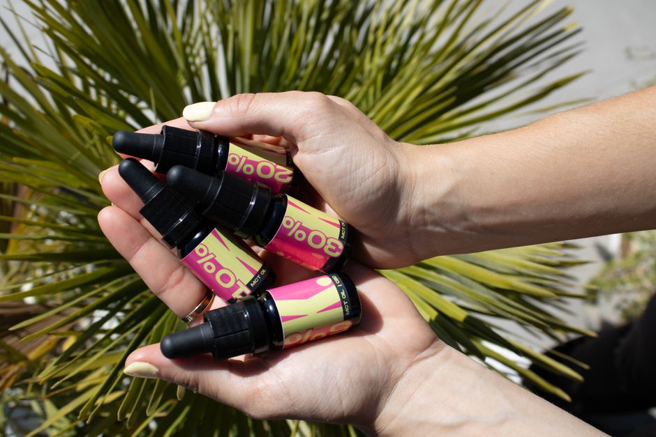 Hands gently holding wellness dropper bottles against a vibrant green plant backdrop.