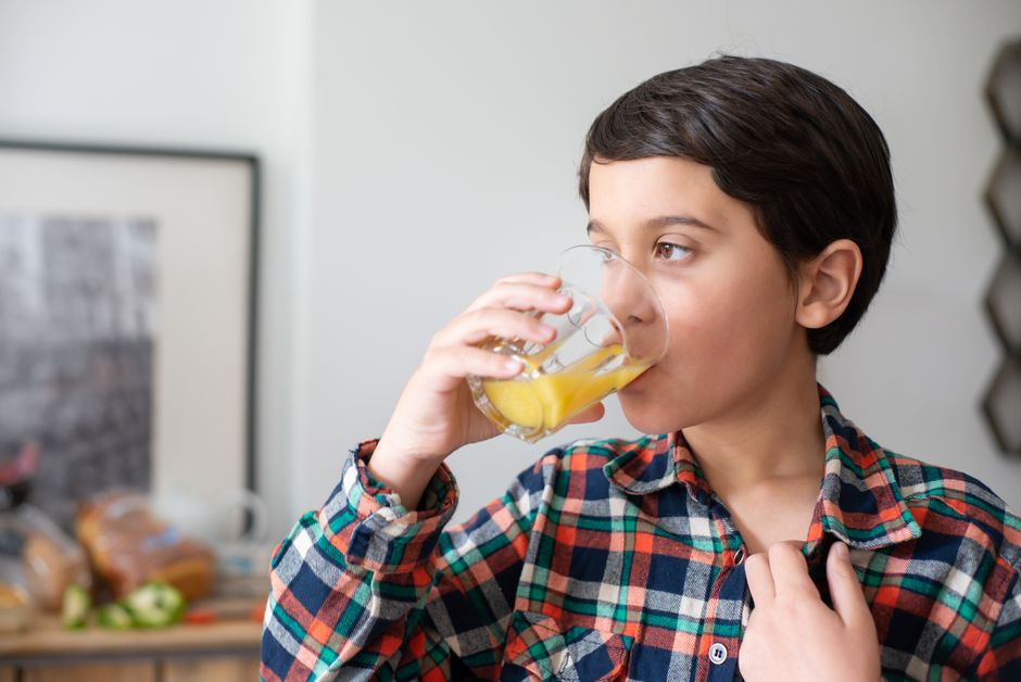 Young boy drinking fresh orange juice in a cozy indoor setting, showcasing healthy lifestyle.