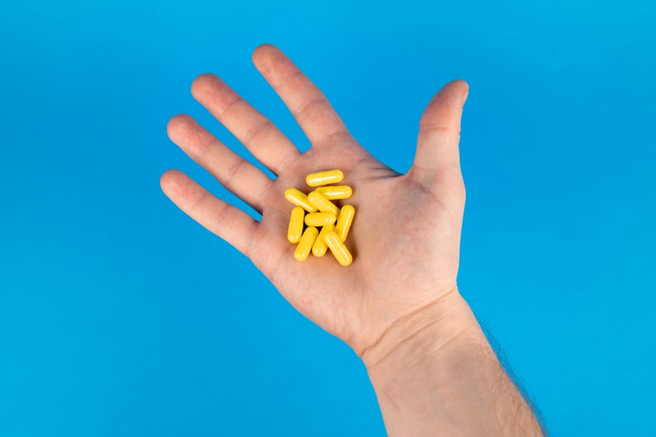 A close-up of a hand holding yellow capsules against a vibrant blue background.